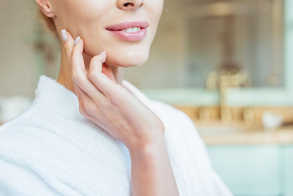 cropped shot of beautiful smiling woman in bathrobe touching face with perfect skin