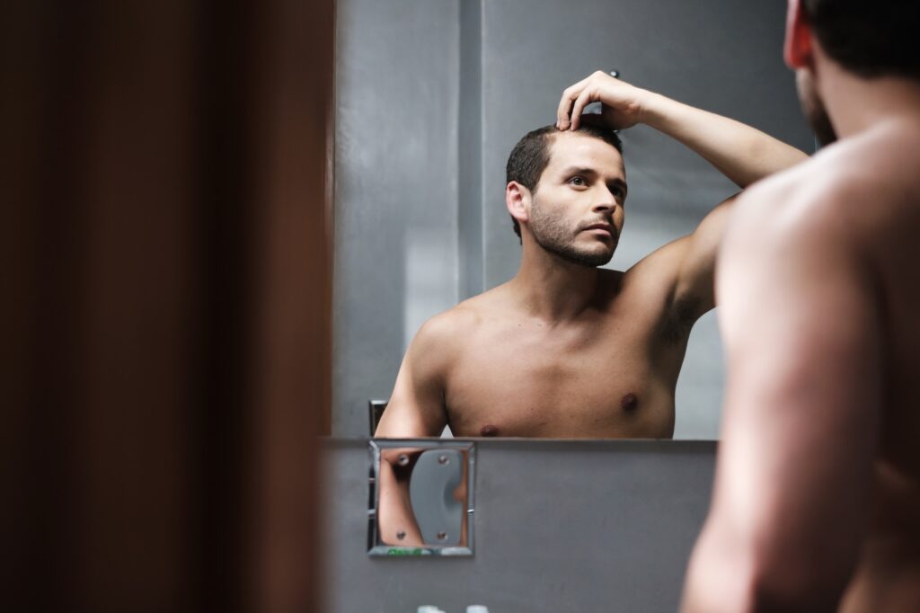 Young Man In Bathroom Worried About Premature Receding Hairline